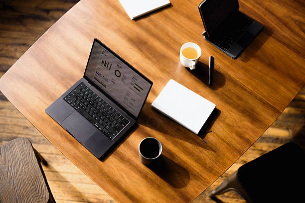 Wooden table with laptop displaying charts and graphs, teacup, notebook, and tablet, ideal for business and technology concepts