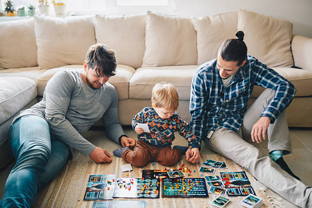 Two men and a 2 year old boy playing a board game. Two men bonding with a child.