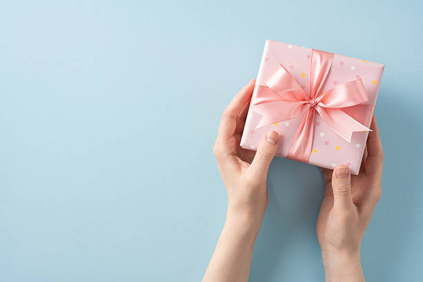 istock Gift box with a pink bow held by hands against a pastel background 2213974270