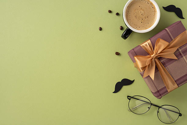 istock Flatlay with a gift box wrapped in ribbon, coffee cup, eyeglasses, and moustache decor on a green background conveying celebration and sentiments 2213974271