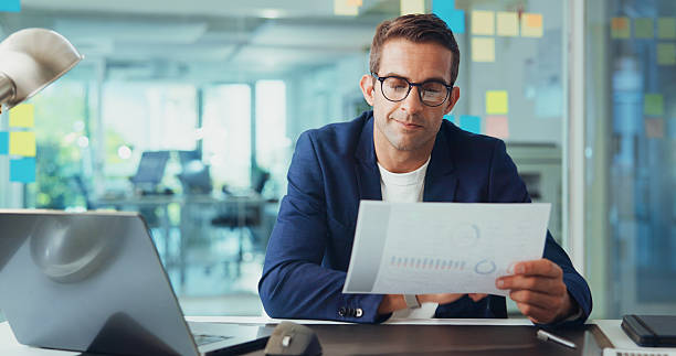 istock Businessman, documents and reading statistics with laptop for company performance or report at office. Man, employee or financial analyst with paperwork for business growth or analytics at workplace 2213978889