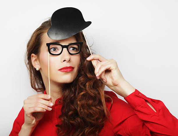 Cute Little girl having fun and posing in a homemade Photo Booth that her family made for her birthday party. Photo Booth made of curtains, ribbons, and string lights and empty photo frames. The little girl is holding a glasses/mustache prop on a stick. Photo in black and white.