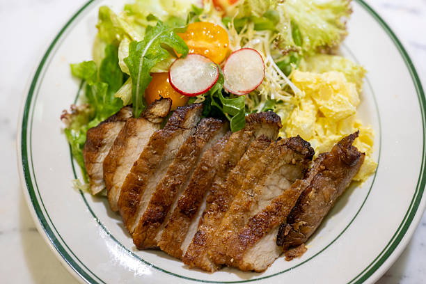 A delectable grilled pork chop served alongside a vibrant salad, featuring radishes and cherry tomatoes, presented on a white plate with green rim accents. The dish exudes freshness and simplicity, ideal for culinary presentations or food marketing materials.