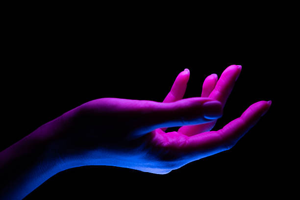 An elegant female hand in dramatic lighting with vibrant neon pink and blue tones on a black background, creating a striking and futuristic contrast. This image evokes concepts of creativity and innovation.