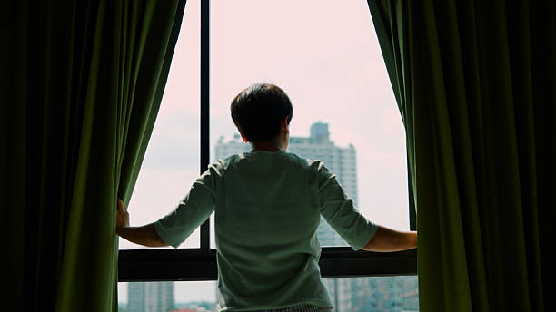 istock Asian woman looking through window 2213997114