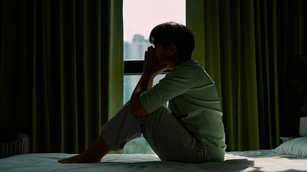 istock Asian woman sitting on bed and looking through window 2213997136