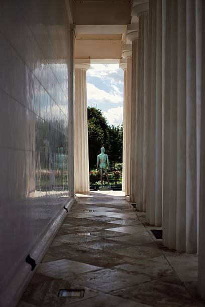Green backwards-facing human statue at the end of a pillared white building