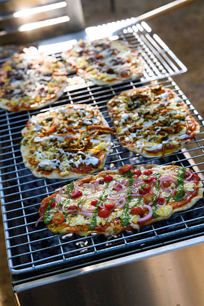 Outdoor barbecue session featuring homemade artisan pizzas topped with fresh ingredients like tomatoes, onions, and herbs. This delightful cooking method on a grill highlights the crispy crust and melted cheese, perfect for al fresco dining. An exceptional image to illustrate outdoor cooking and family picnics.