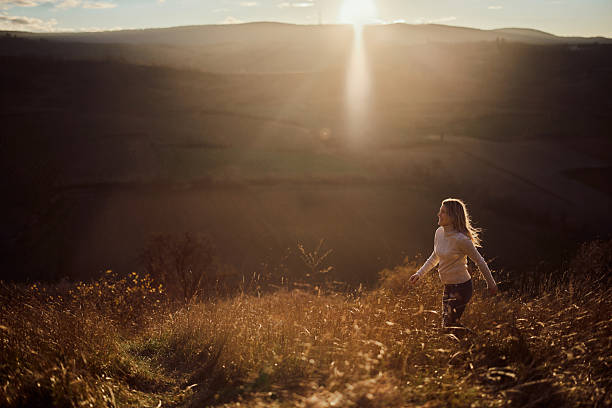 Happy woman having fun while running through tall grass during autumn sunset on a hill. Copy space.
