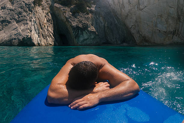 Attractive man relaxing and sunbathing on a board and floating on beautiful clear sea water