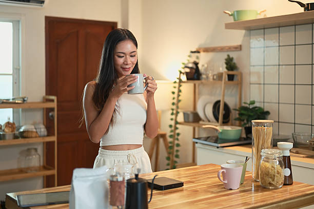 istock Smiling woman savoring a warm cup of coffee while standing in a cozy, modern kitchen 2214008736