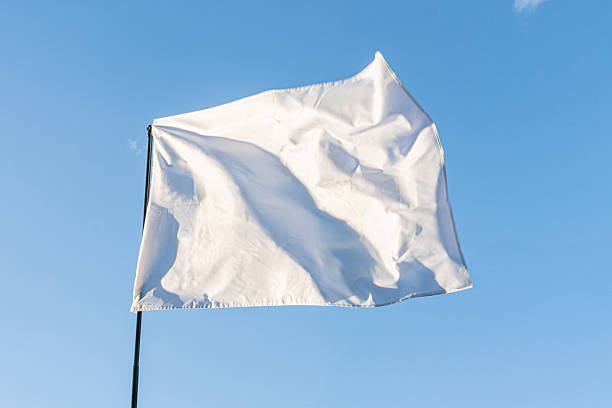 istock White flag with creases, off-center in frame, casting a shadow on clear blue sky, light source from above No specific location, event or time period evident Perspective from below looking up at the 2214009232
