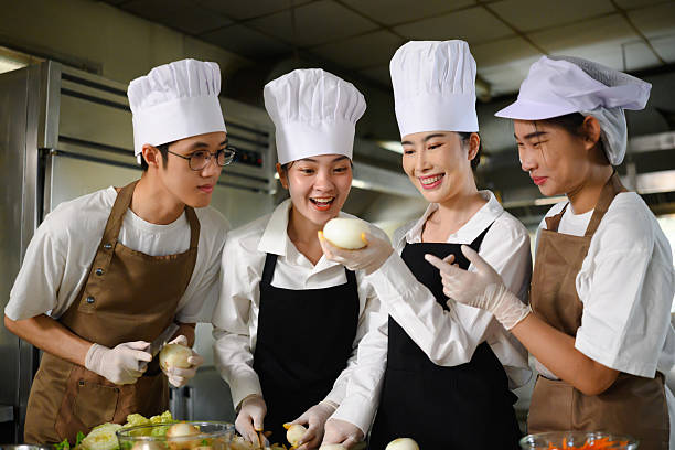 Group of culinary students in uniform learning food preparation in a professional kitchen.