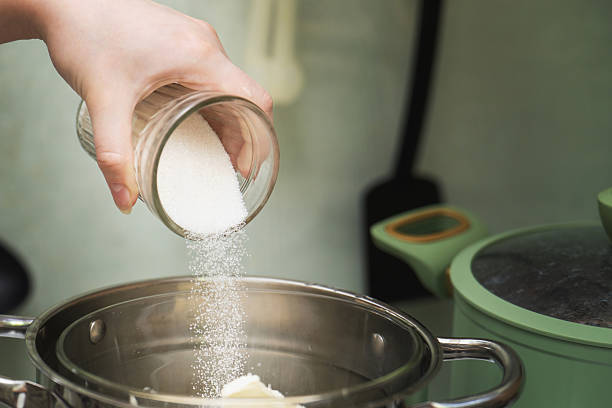 istock Granulated sugar being poured from a glass into a metal cooking pot, capturing a precise baking ingredient measurement 2214013540