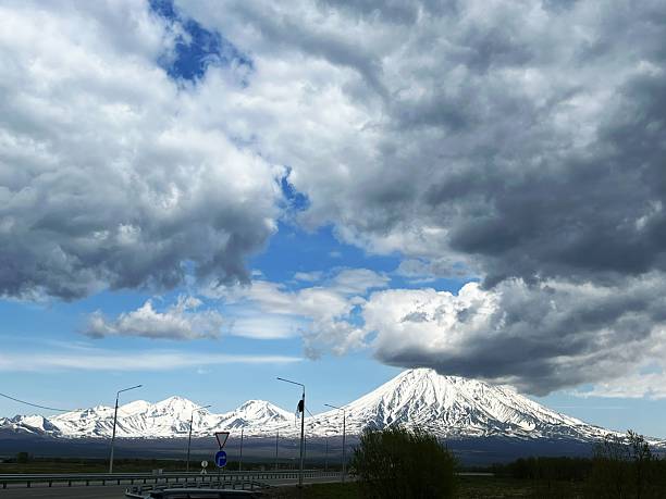 Snow-capped volcanoes under dramatic cloudy sky in scenic landscape.