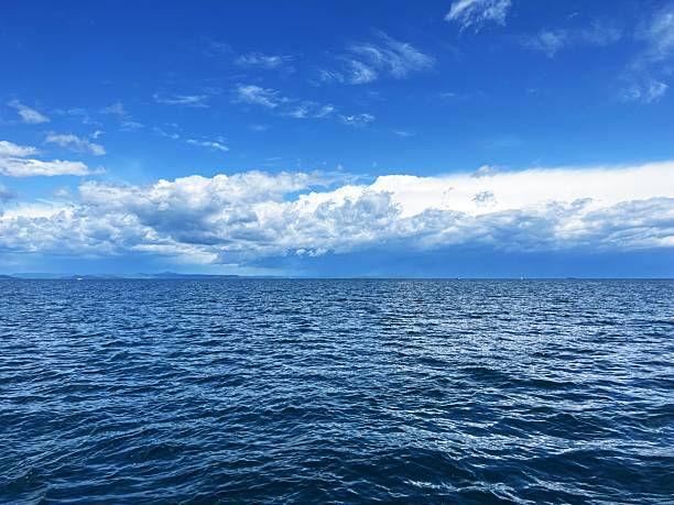 Vast ocean under clear blue sky with white clouds on a calm day.