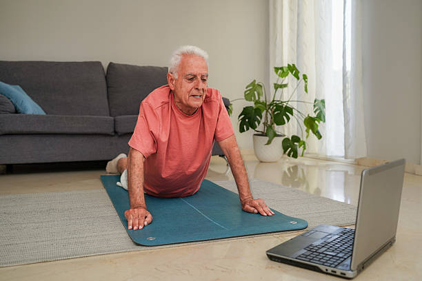 istock Senior man practicing yoga on mat with a laptop at home 2214018513