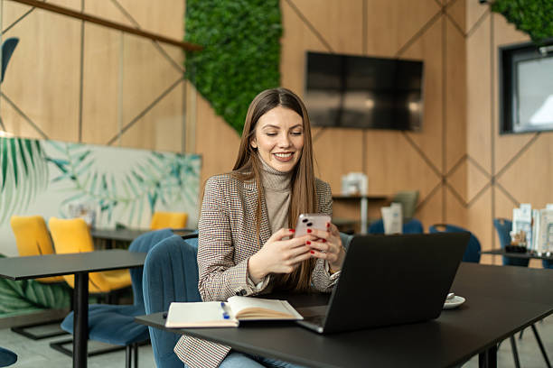 istock Young businesswoman using smartphone and working on laptop in modern cafe 2214021944