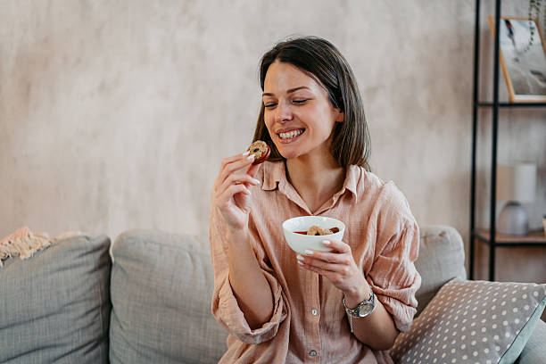 istock Young Woman Eating Cookies While Sitting On The Sofa 2214021958
