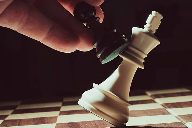 istock Black pawn knocking down white king on chessboard 2214023216