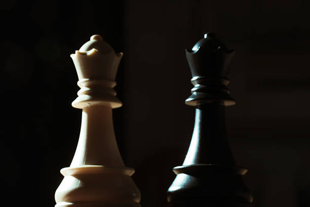 White and black queen chess pieces stand facing each other, creating a dramatic contrast against a dark background, symbolizing strategic gameplay