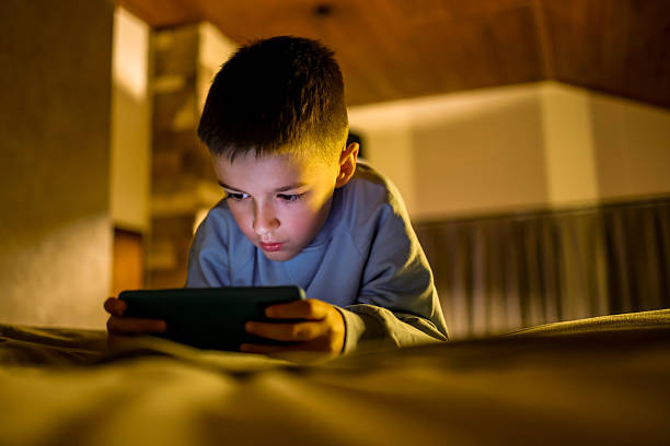 istock Young Boy Focused on Using a Tablet in a Dimly Lit Room 2214023926