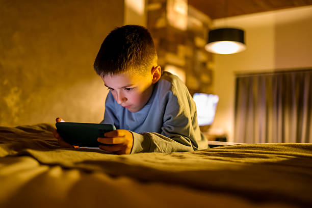 istock Young Boy Playing on Smartphone While Lying in Modern Bedroom 2214023945