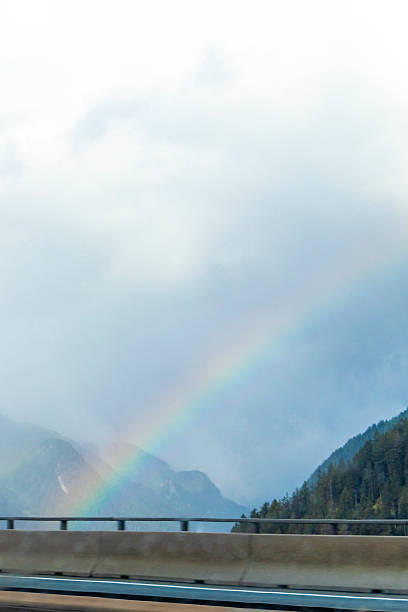 Rainbow at mountain landscape mountains green fields forest clouds and blue sky in the Alps Tyrol Austria.