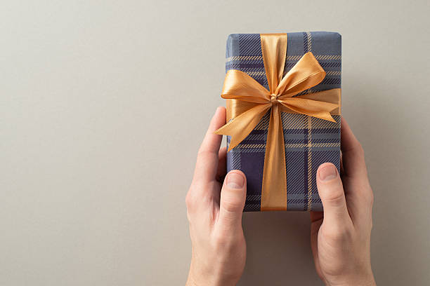 istock A wrapped gift box with a plaid pattern held by hands, featuring a golden ribbon bow 2214025566