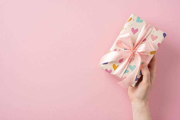 istock Colorful gift wrapped with heart-patterned paper and pink ribbon held on pink backdrop 2214025575