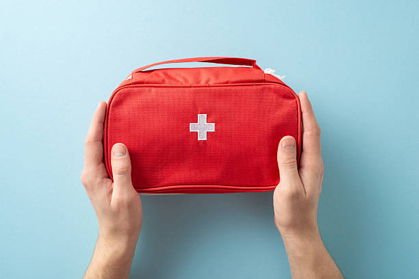 istock Red first aid kit held by two hands on a clean light blue background showcasing care 2214025577