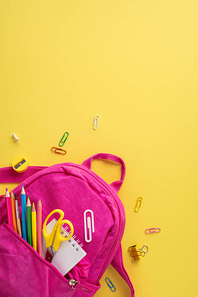 istock Pink vertical backpack filled with school supplies on a bright yellow background, arranged creatively 2214025599