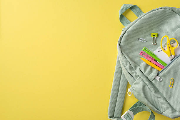istock Green backpack with school stationery including scissors and pens on a bright yellow background 2214025662
