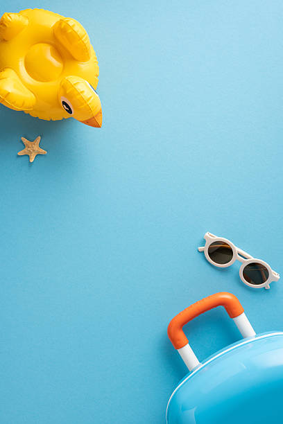 istock Stylish vertical summer accessories including a duck float, sunglasses, and suitcase on blue backdrop 2214025693