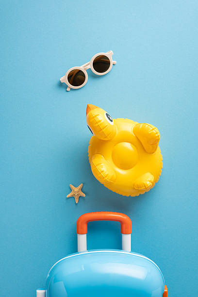 istock Top vertical view of summer-themed essentials on a blue background, featuring a suitcase, sunglasses, inflatable duck, and starfish, ideal for concepts of travel, summer holidays, and relaxation vibes 2214025696