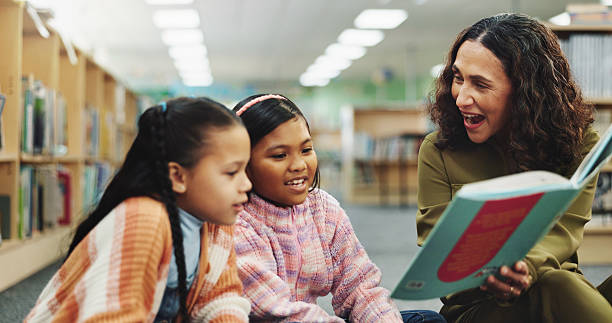 istock Children, teacher and education with reading book at library for development, learning or study with guide. School kids, storytelling and woman with help, excited or language for knowledge at academy 2214027172