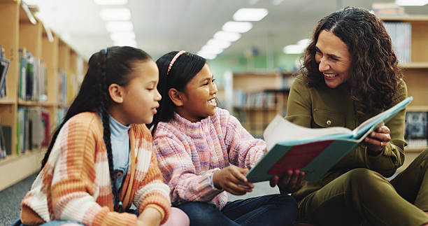 istock School kids, teacher and happy with book at library for development, learning and education on floor. Children, reading and storytelling with woman for help, excited or teaching language at academy 2214027177