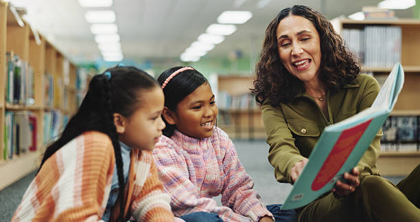 School kids, teacher and education with book at library for development, learning or study with guide. Children, reading and storytelling with woman for help, excited or teaching language at academy