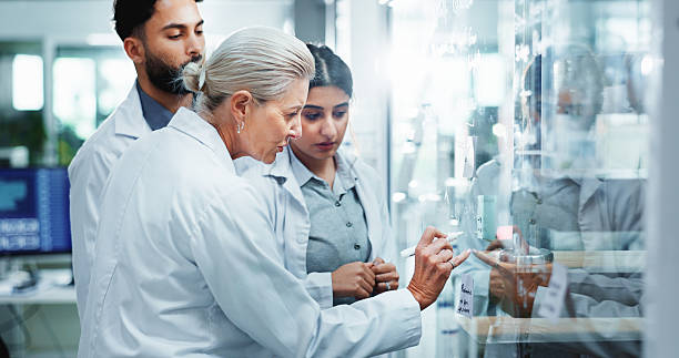 istock Glass wall, science and people in lab, research and collaboration for experiment. Scientist, group and employees in workplace, cooperation and review chemistry equation with brainstorming and results 2214027435