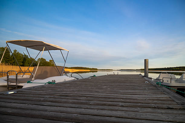 A small boat rests beside a wooden dock as the warm glow of evening light reflects on a calm, glassy lake.