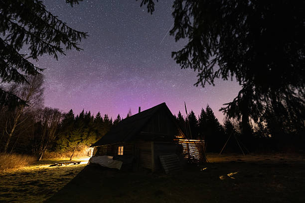 istock A forest cabin with a light in the window under a starry sky and beautiful violet-blue Northern Lights. 2214032004