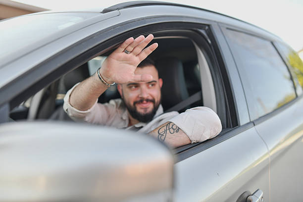 istock Man Driving With Open Window Waves Warmly at Familiar Face 2214036531