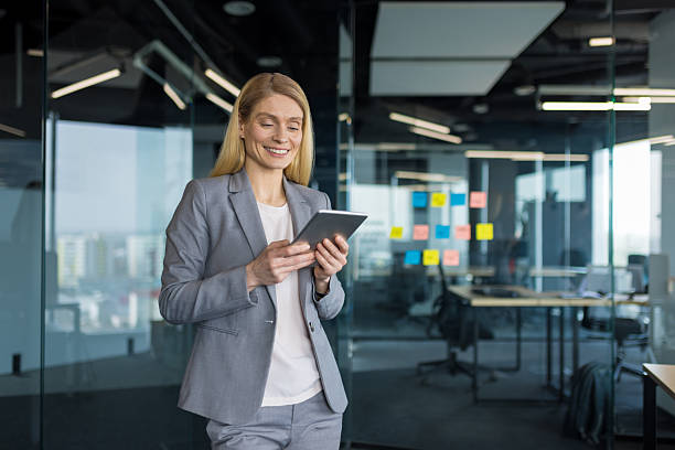 istock Successful woman in business suit standing inside office with tablet computer in hands smiling happily. Happy businesswoman reading electronic report and viewing investment data online 2214036963