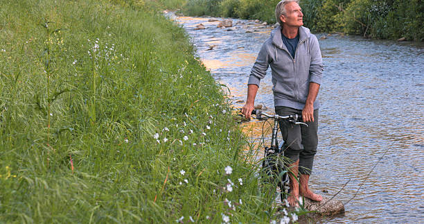 istock Mature man on riverbank with bicycle 2214040694
