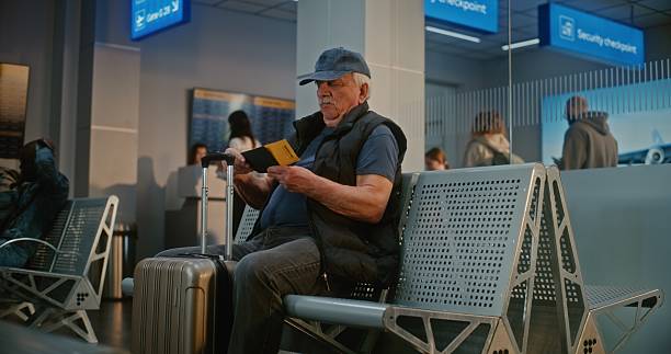istock Airport Terminal: Senior Man with Suitcase and Passport Sitting in Departure Hall After Security Check 2214043367