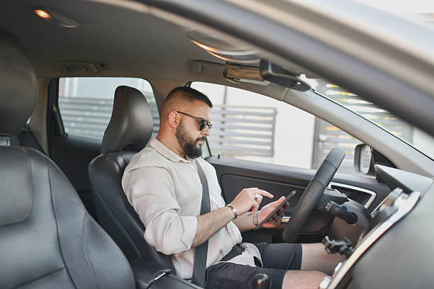 istock Male Driver Responding to Text Messages on Phone While Sitting in Parked Car 2214047132