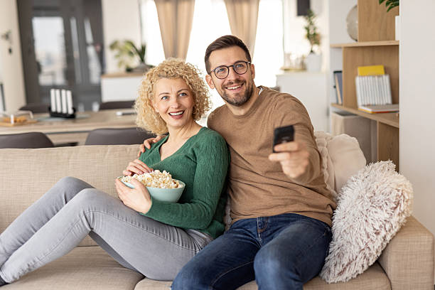 istock Cheerful couple watching TV with popcorn in their hands. 2214048113