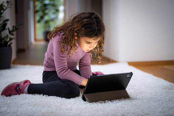 istock Young Girl Concentrating on Tablet While Sitting on Carpet 2214049930