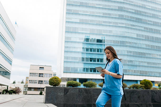 istock Young nurse walking and using digital tablet in front of hospital 2214052489