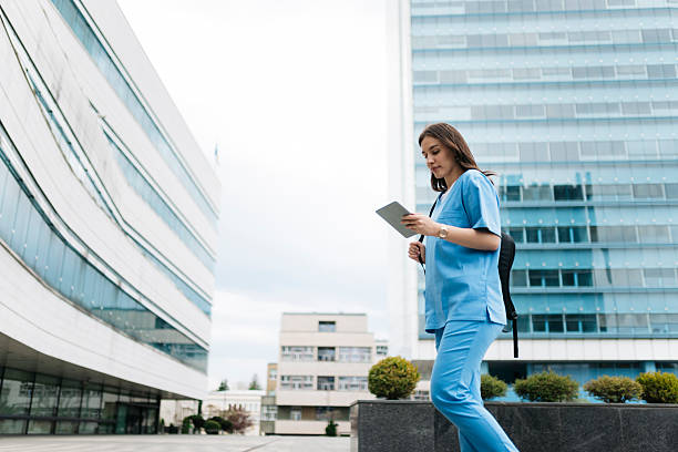 istock Young doctor walking and using digital tablet in front of hospital 2214052491